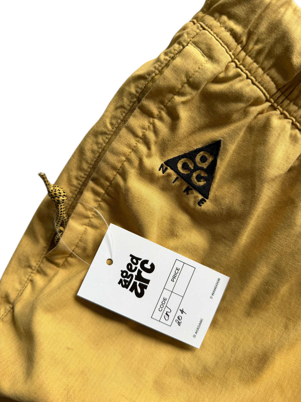 Aged Arc mustard yellow Nike ACG shorts with an elastic waistband and drawstring detail.
